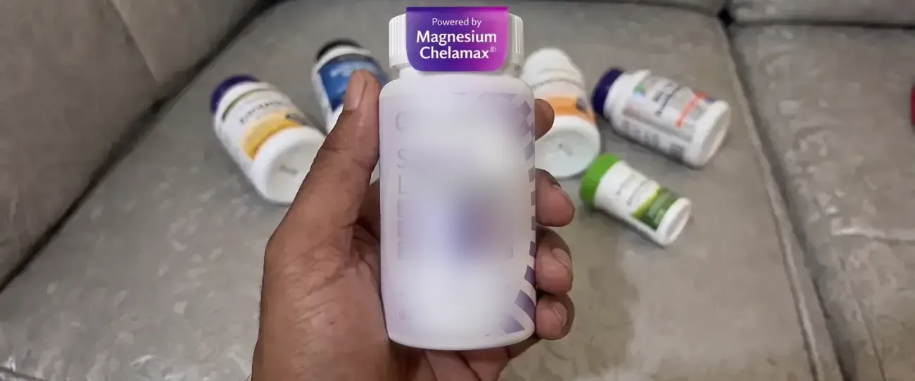 A hand holding the Evolance Calm+Rest bottle above the half-used bottles on the couch — the front label is blurred, only the cap band reading Powered by Magnesium Chelamax is legible
