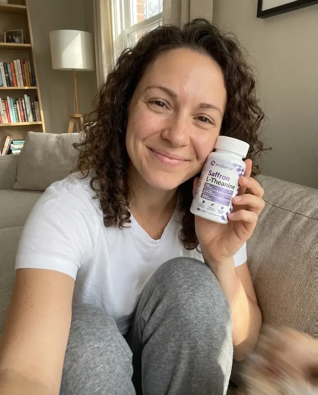 A reader on her couch at home, holding the Evolance Calm+Rest bottle